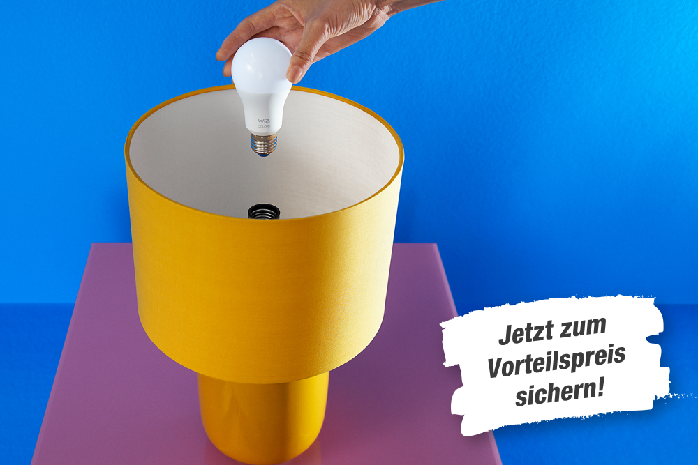 Hand schraubt Glühbirne in gelbe Tischleuchte